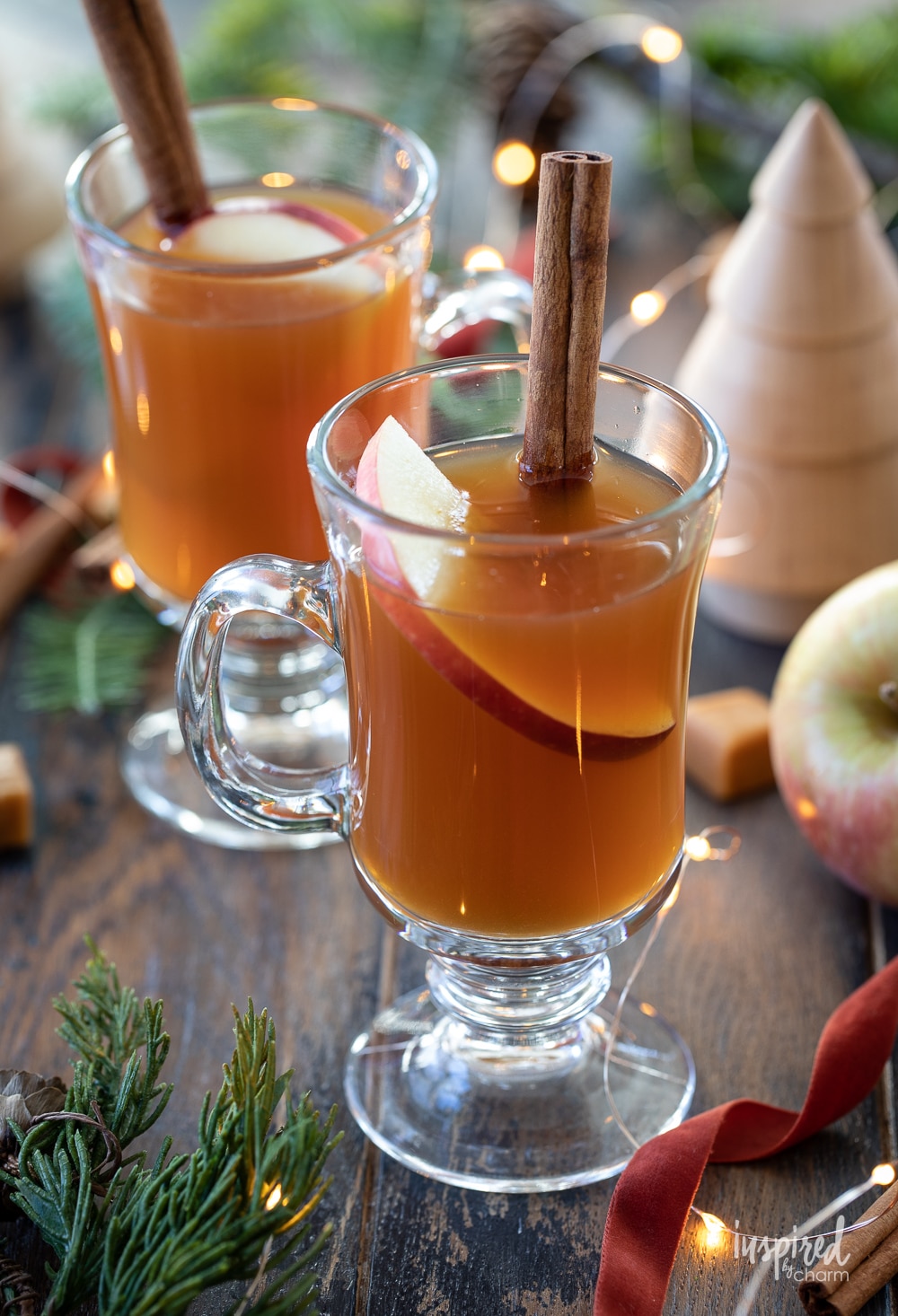 two glasses of spiked caramel apple cider tea garnished with apples and cinnamon sticks.