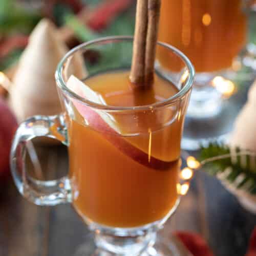clear glass of spiked caramel apple cider tea in a glass with a cinnamon stick.