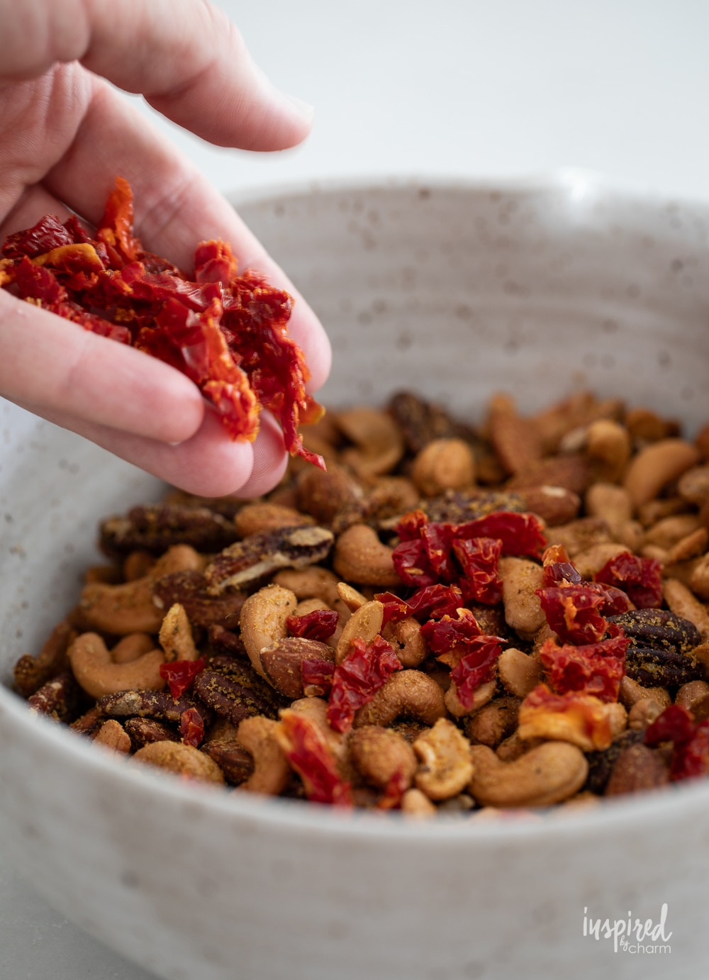 hand adding sun-dried tomatoes to pizza trail mix. 