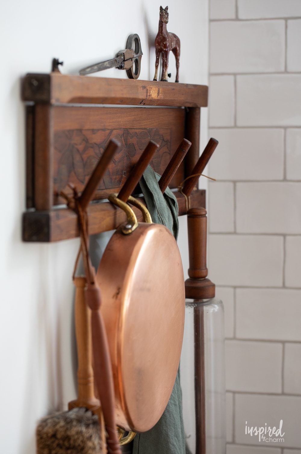 close up of a vintage wood rack hung on a wall with copper pan, rolling pin, and an apron.