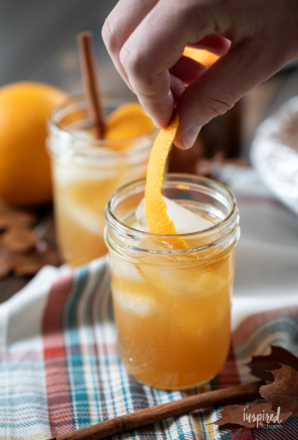 hand adding orange peel to cocktail in a jar.
