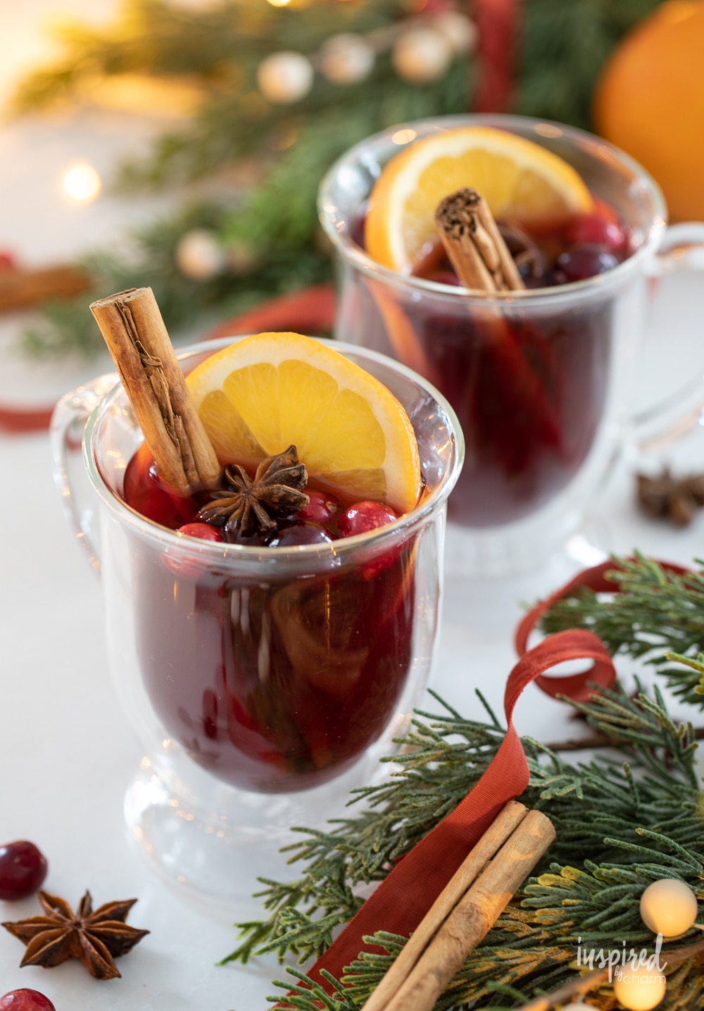 spiced cranberry hot toddies in glass mugs with holiday decor surrounding.