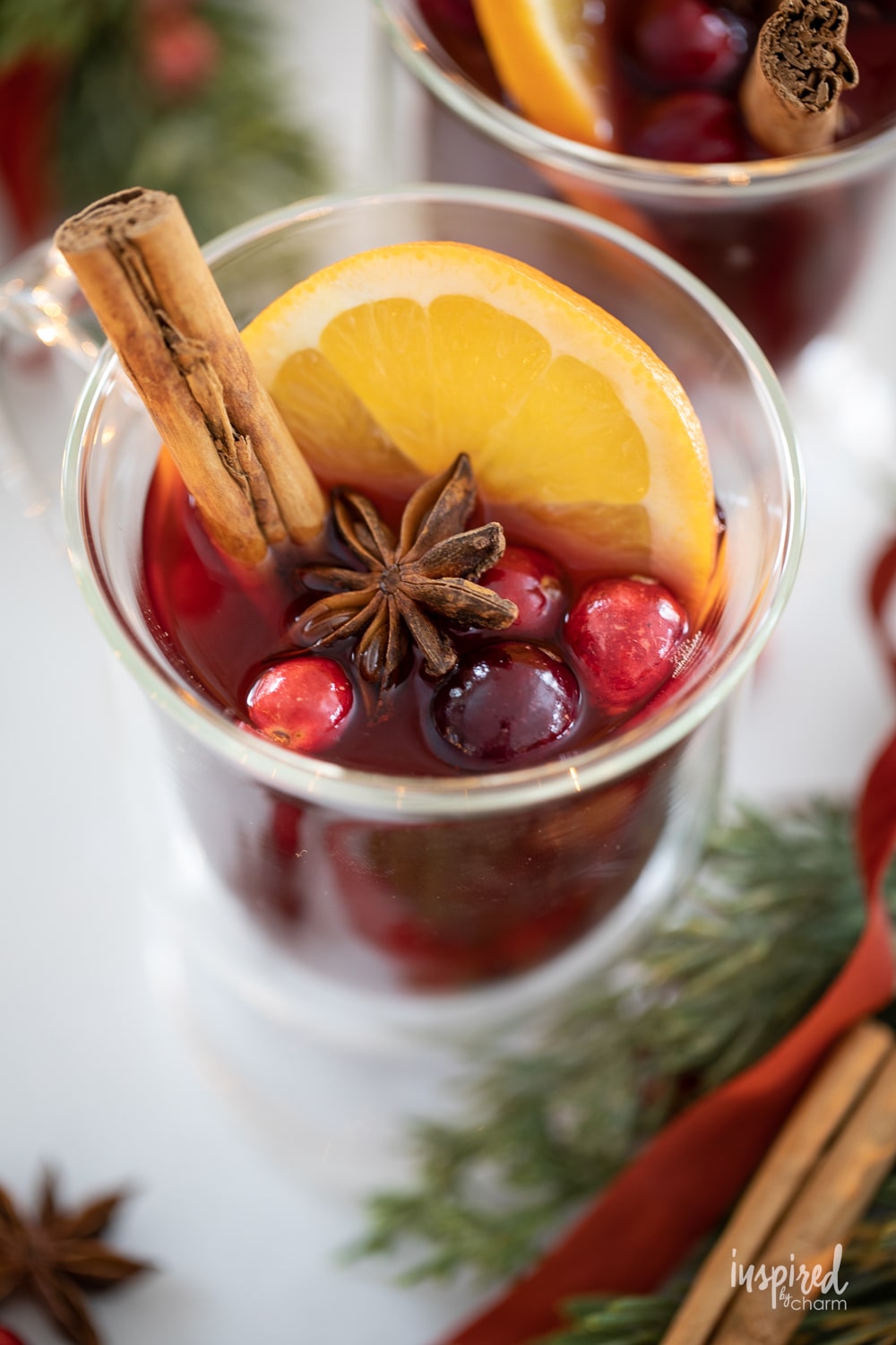 spiced cranberry hot toddy in a glass mugs with cinnamon stick and cranberry garish. 