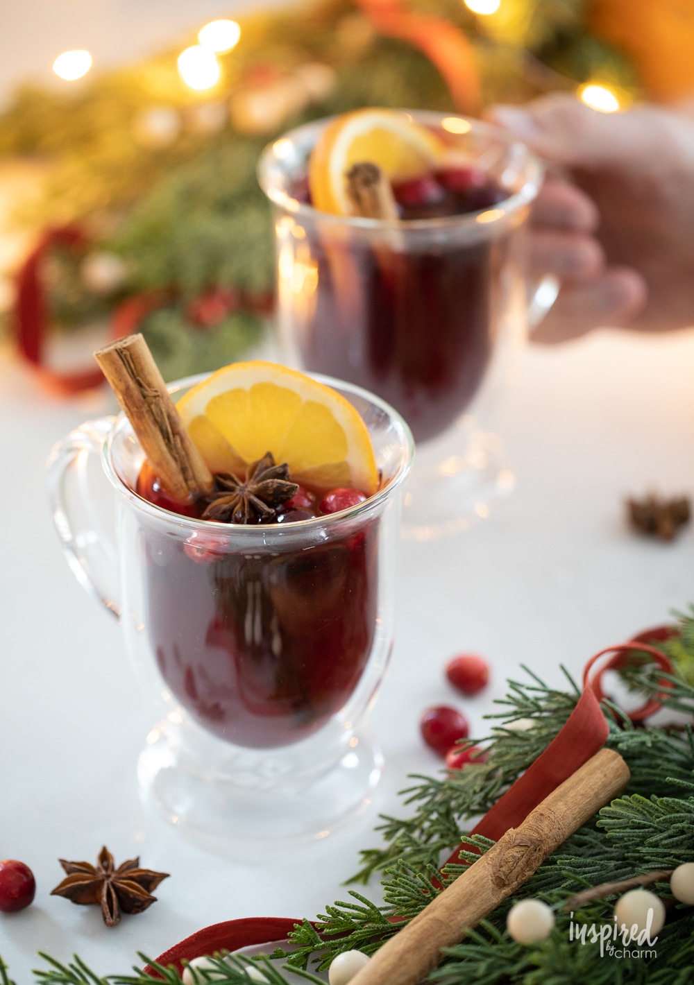 spiced cranberry hot toddies in glass mugs with hand holding one.