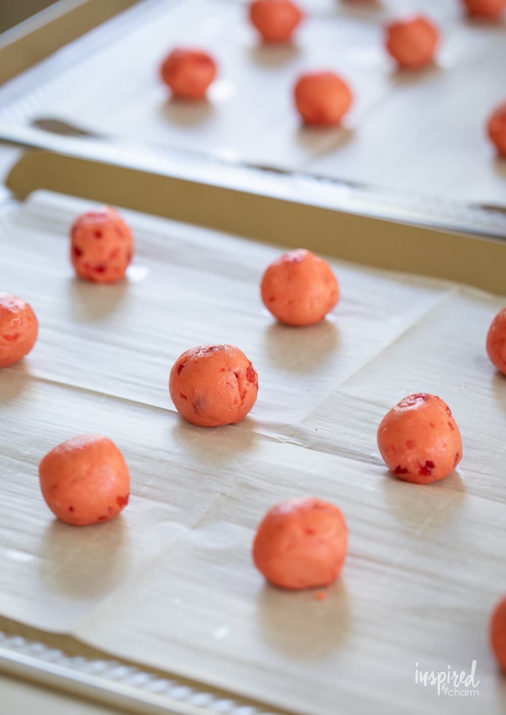 round balls of cherry cookie dough on a parchment lined baking sheet.