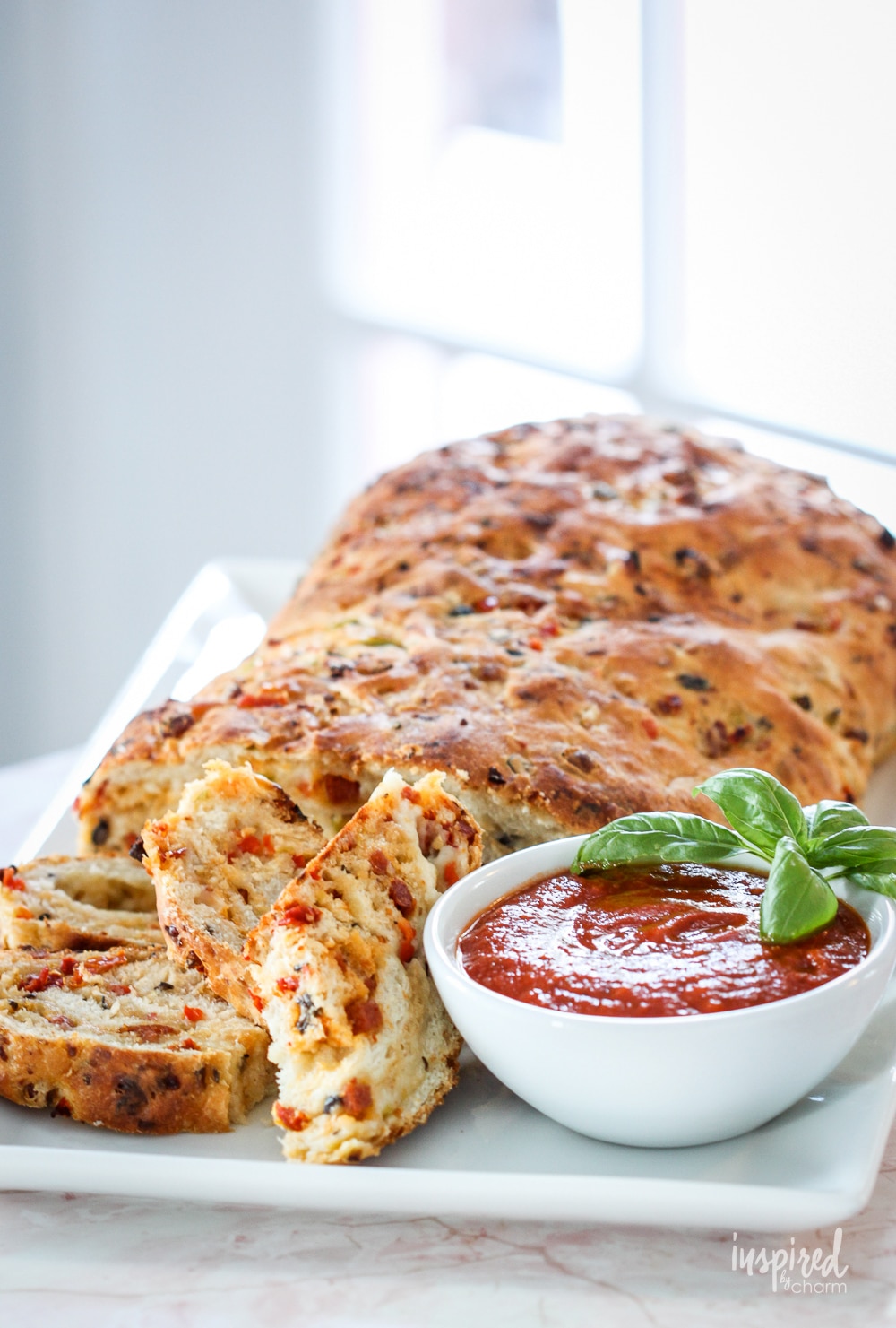 loaf of homemade pizza bread on a platter served with pizza sauce.