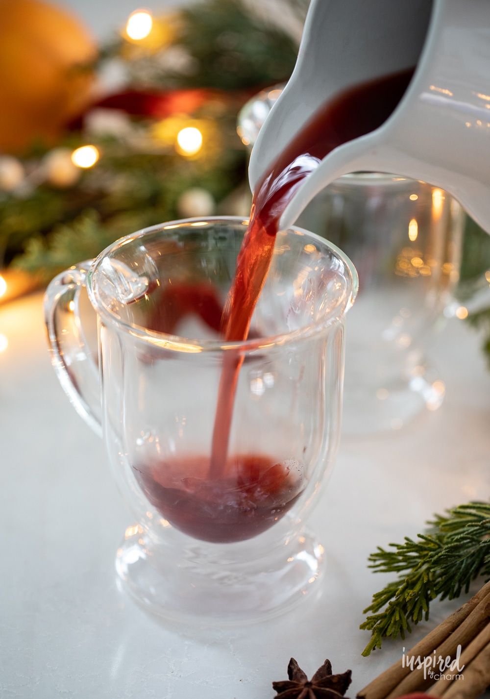 pitcher pouring spiced cranberry juice into glass mug. 
