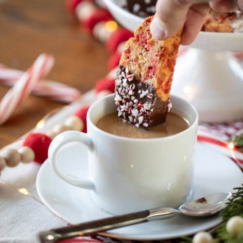 hand dipping a chocolate covered peppermint biscotti into a cup of coffee.