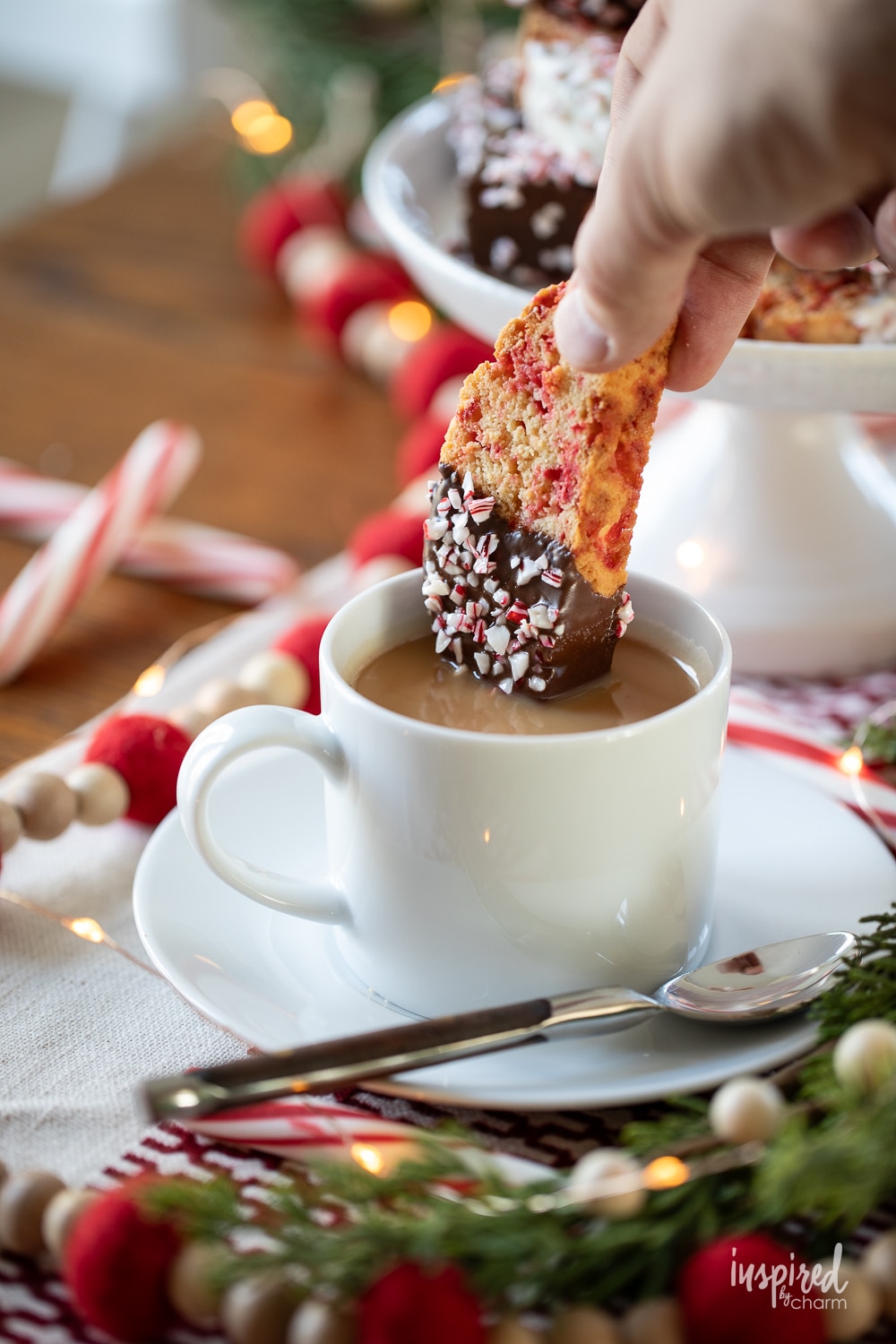 hand dipping a chocolate covered peppermint biscotti into a cup of coffee.