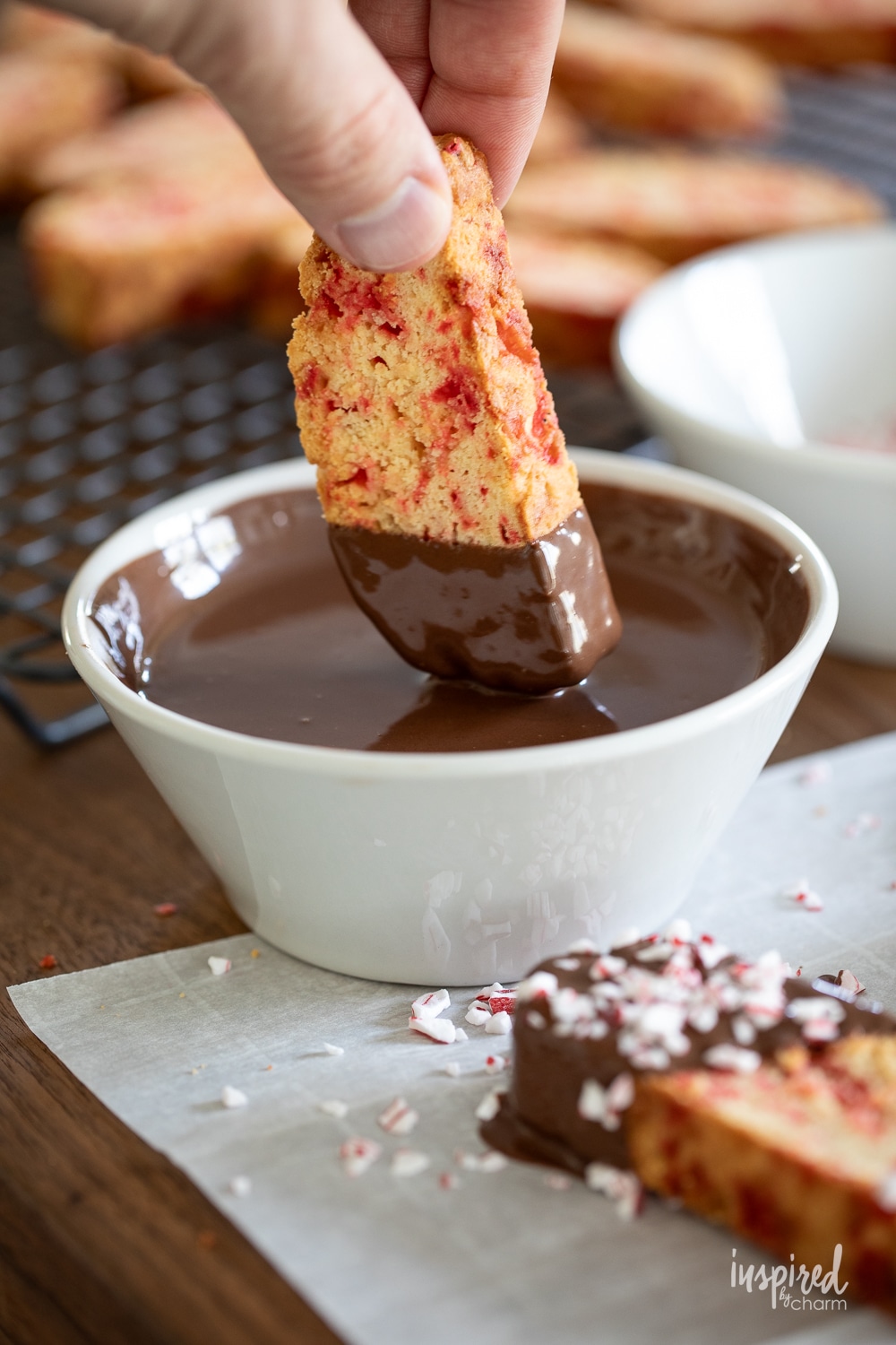hand dipping peppermint biscotti into a bowl of chocolate. 