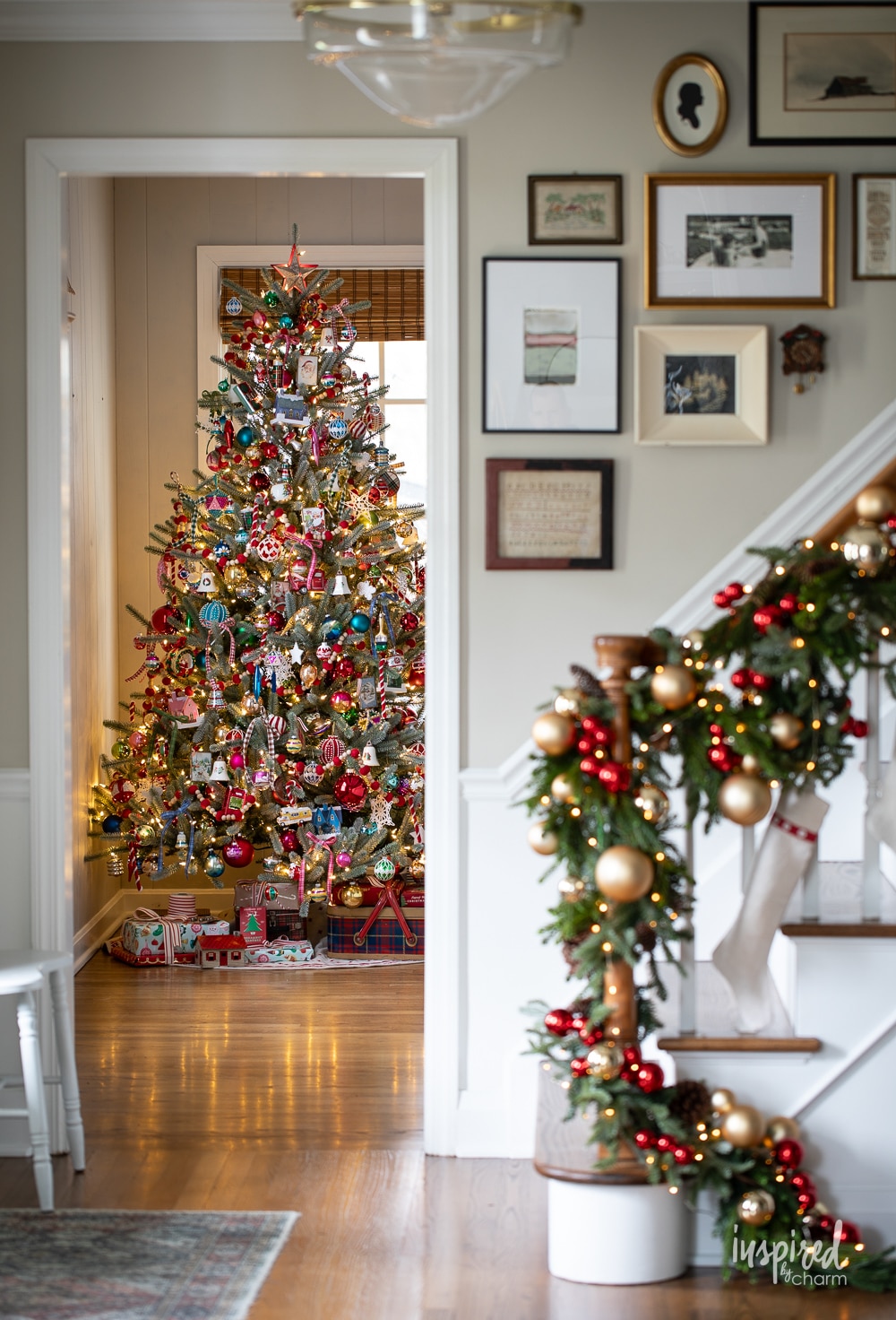 colorfully decorated christmas tree in front of a gallery wall and banister decorated for christmas. 