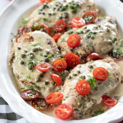 platter of cooked chicken breasts with caper cream sauce on them.