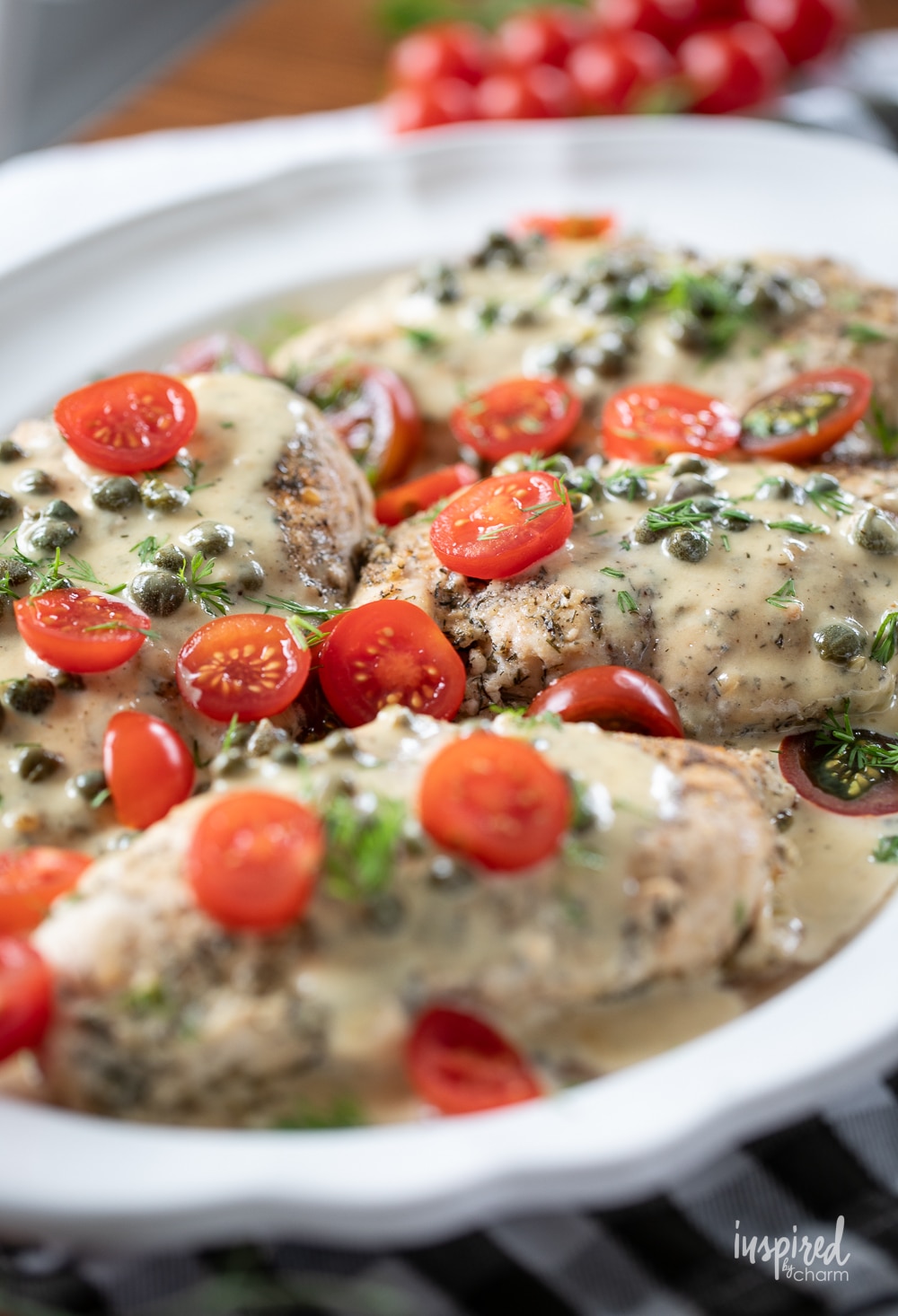 chicken breasts on a platter with tomatoes and cream sauce.