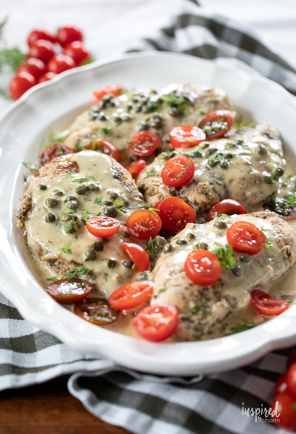 white platter filled with chicken breast covered in a caper cream sauce. 