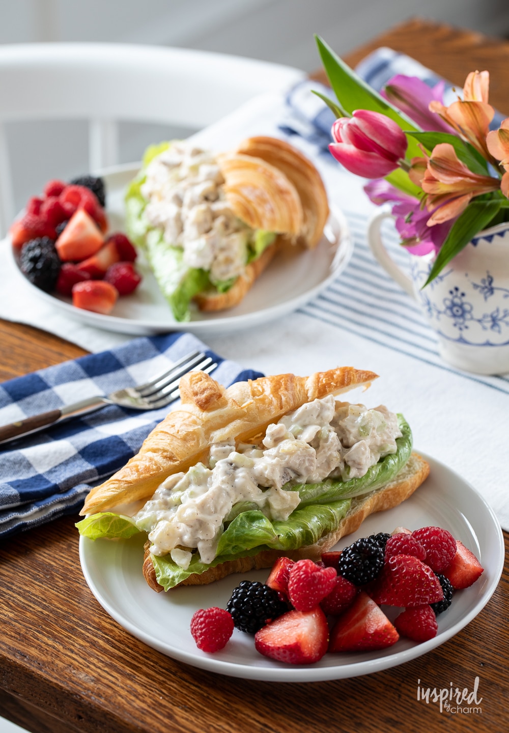 two chicken salad sandwiches served on places with fresh berries. 