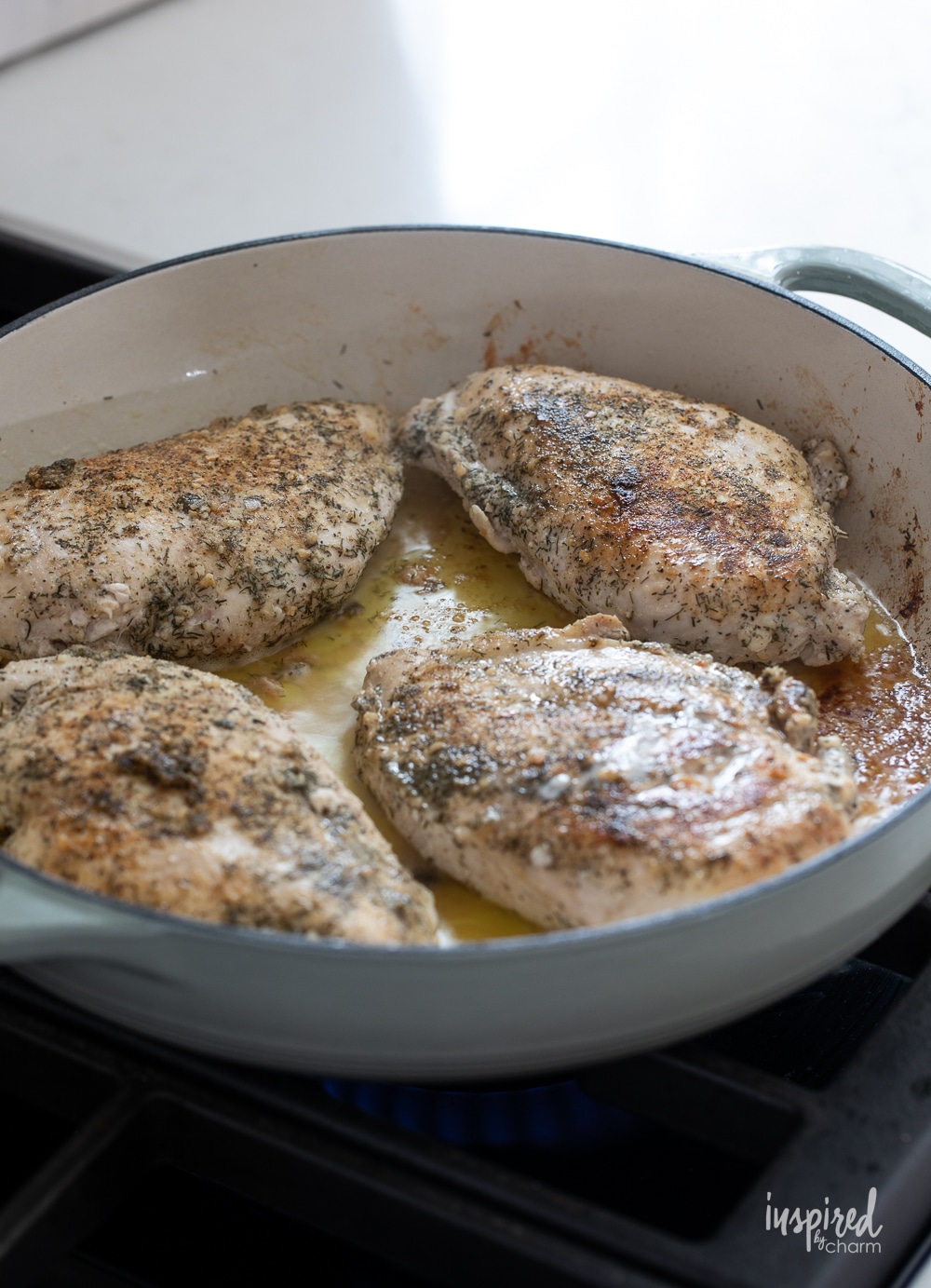 seasoned chicken breasts in a pan cooking.