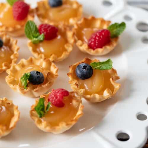 plate filled with lemon curd tartlets topped with fresh berries.