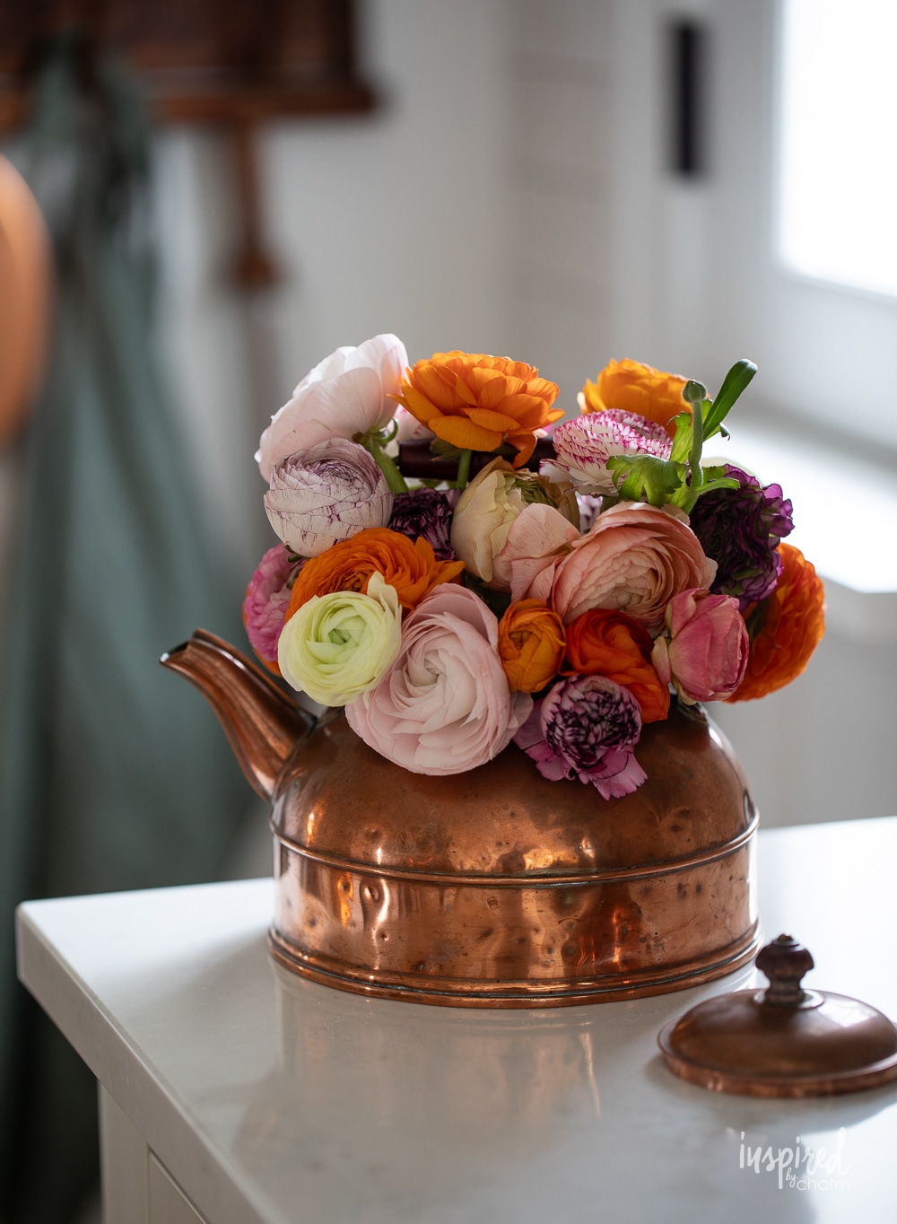 copper teapot filled with colorful ranunculus flowers.