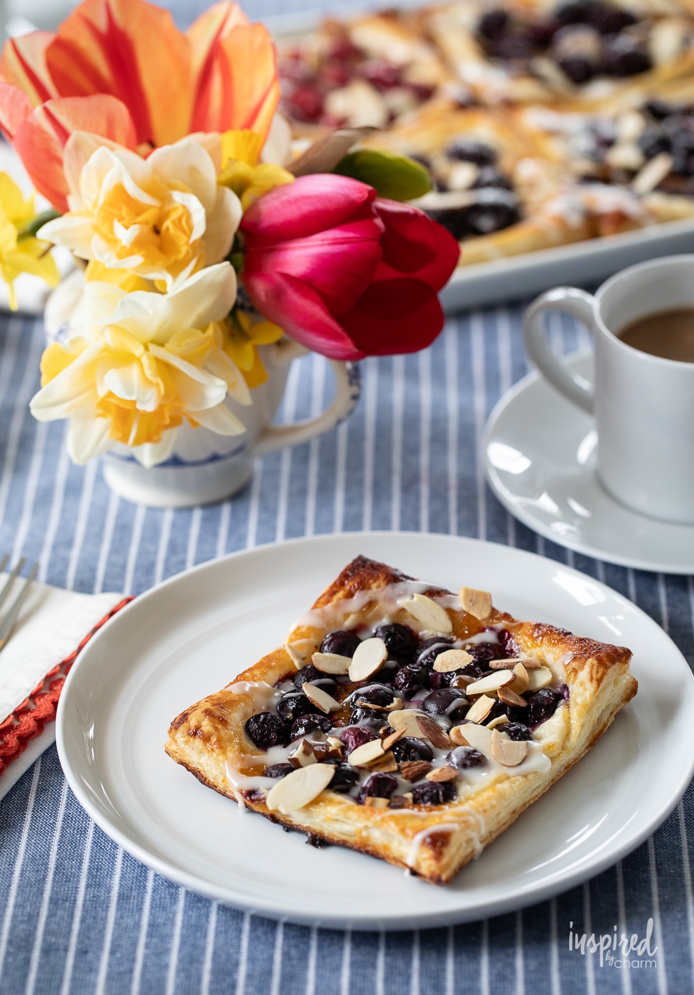 single blueberry and cream cheese danish on a plate with a vase of flowers.
