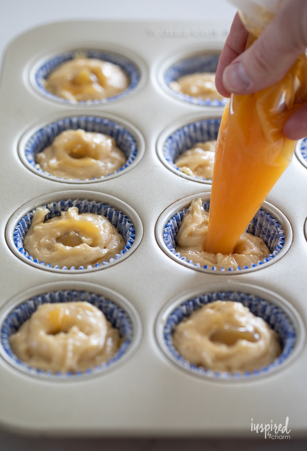 piping bag adding lemon curd to muffin batter in muffin pan. 
