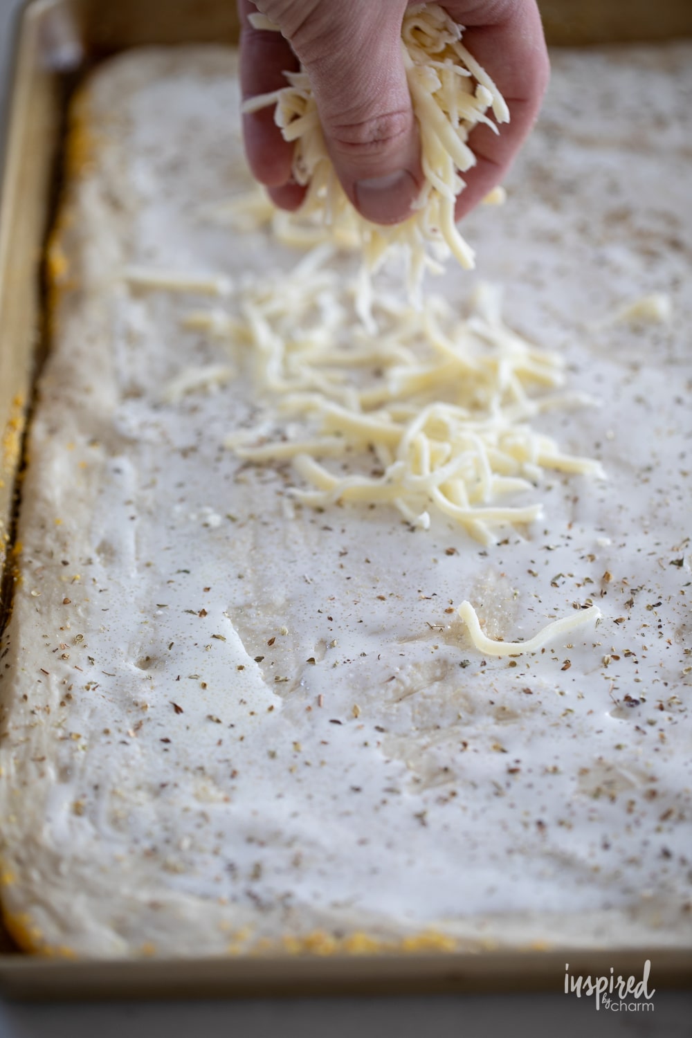 hand adding cheese to pizza dough.