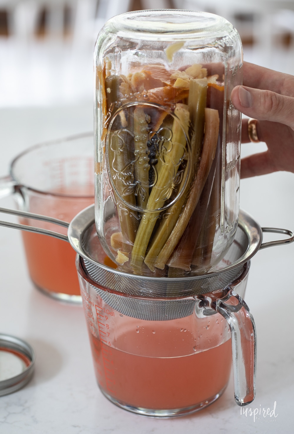 straining homemade rhubarb ginger vodka into a jar.