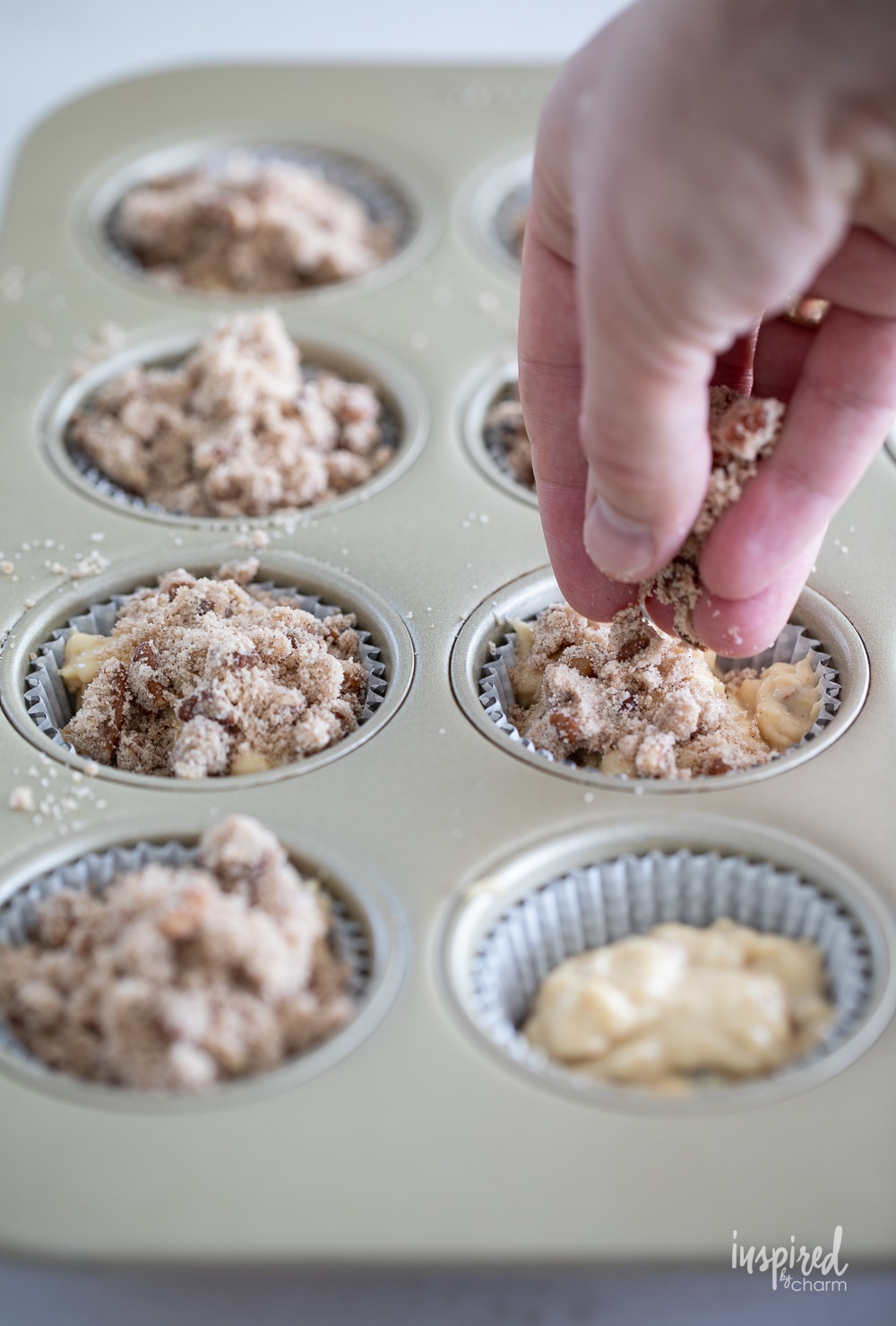 hand adding topping to cinnamon maple morning muffin batter in cupcake pan.