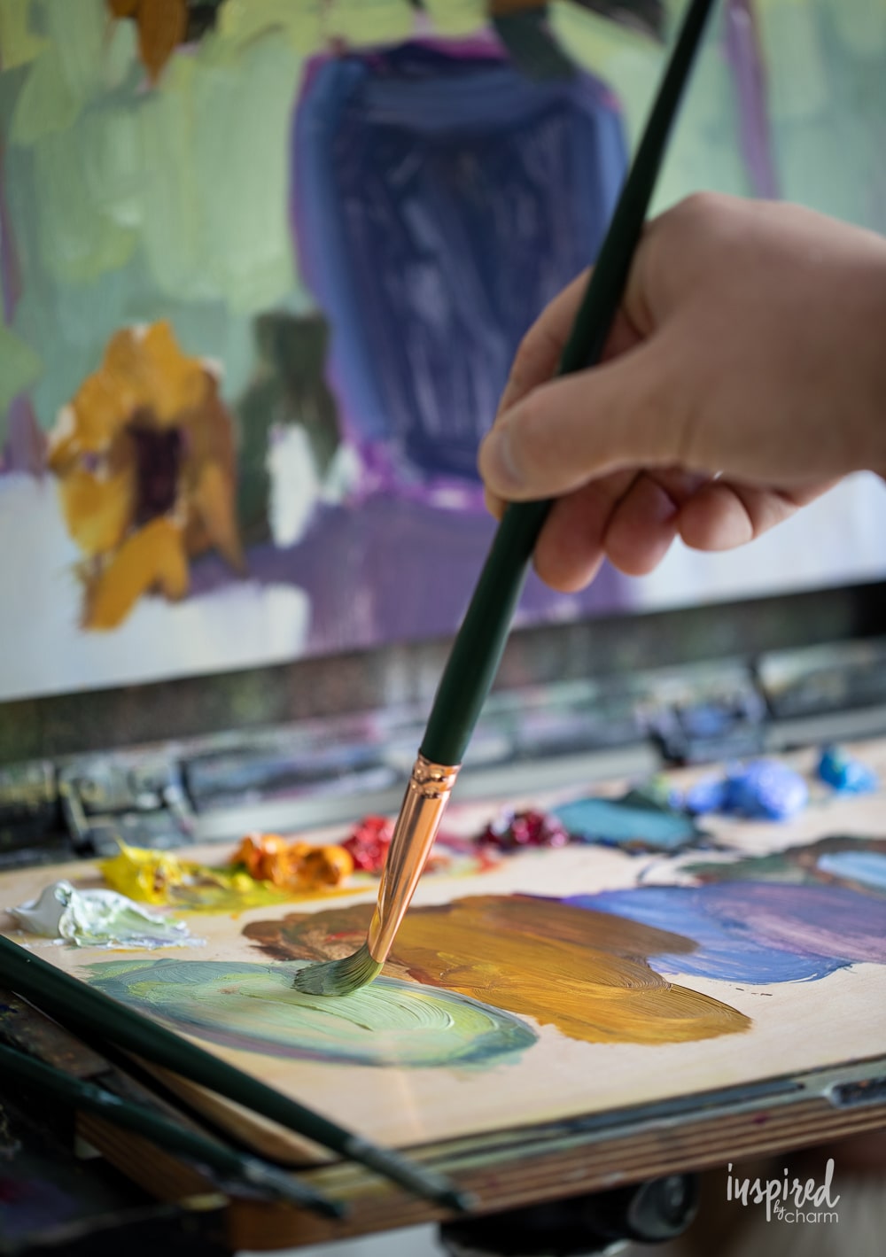 hand with brush mixing oil paints on a palette. 