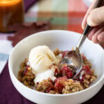 hand with a spoon taking a bit of Plum and Raspberry Crisp with ice cream.