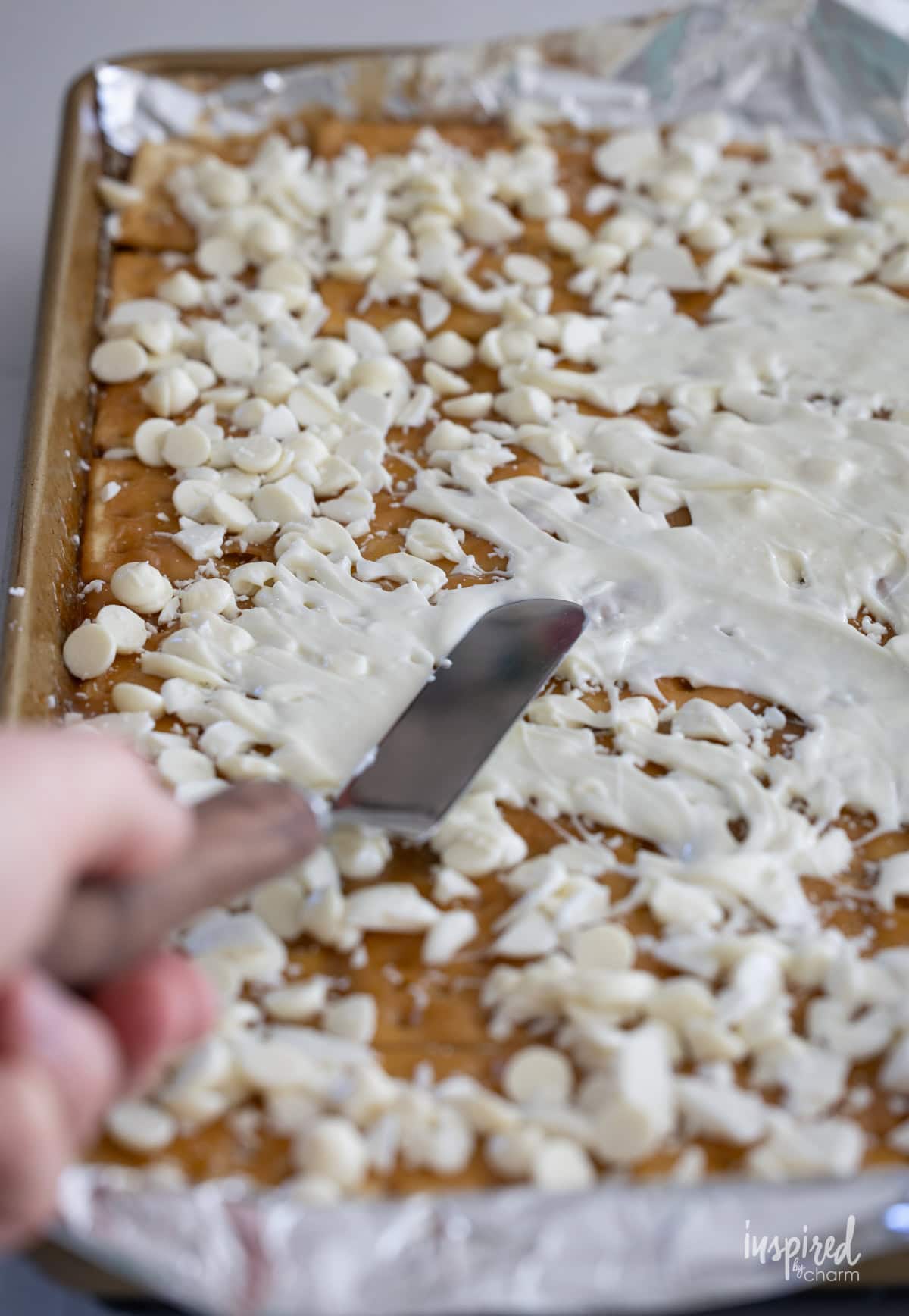 hand with spatula spreading white chocolate over toffee. 