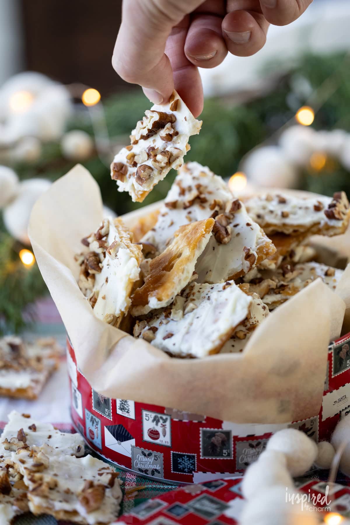 hand taking a piece of Salted White Chocolate Toffee with pecans out of a christmas tin. 