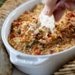 hand with a cracker taking a scoop of Baked Jalapeño Artichoke Dip.