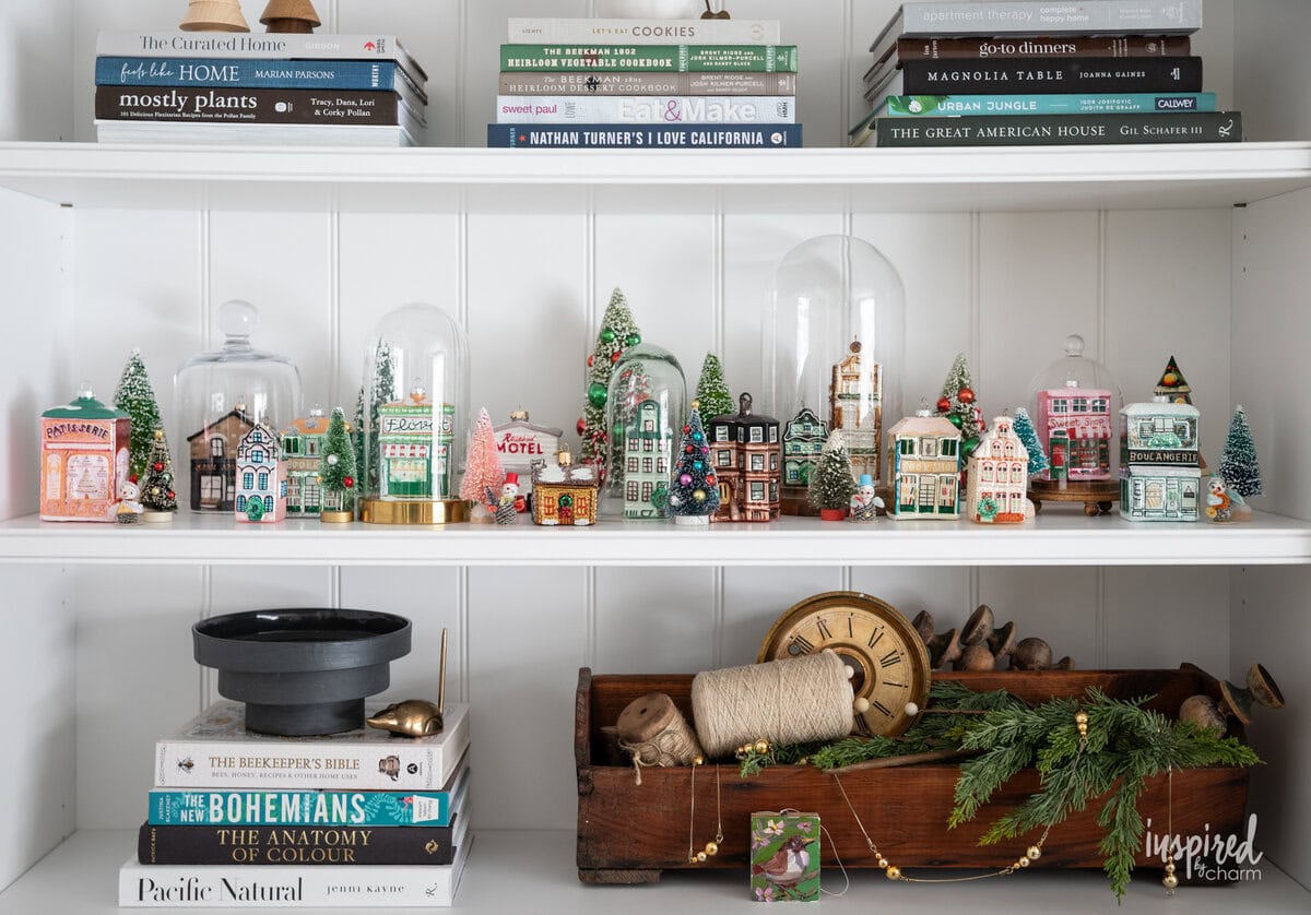 bookshelf with christmas decor and glass house ornament village. 