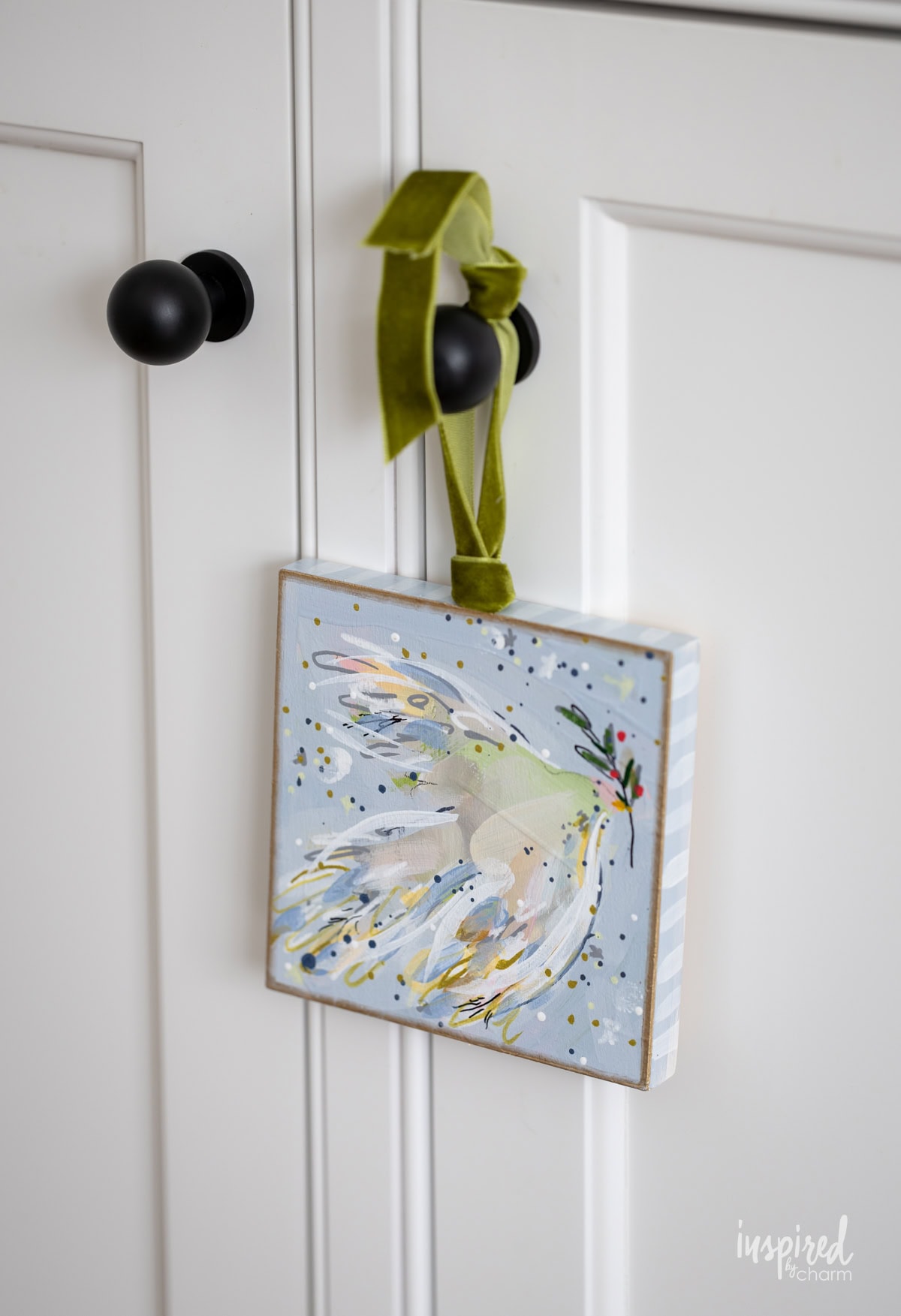 square artwork of a dove hung on a knob.