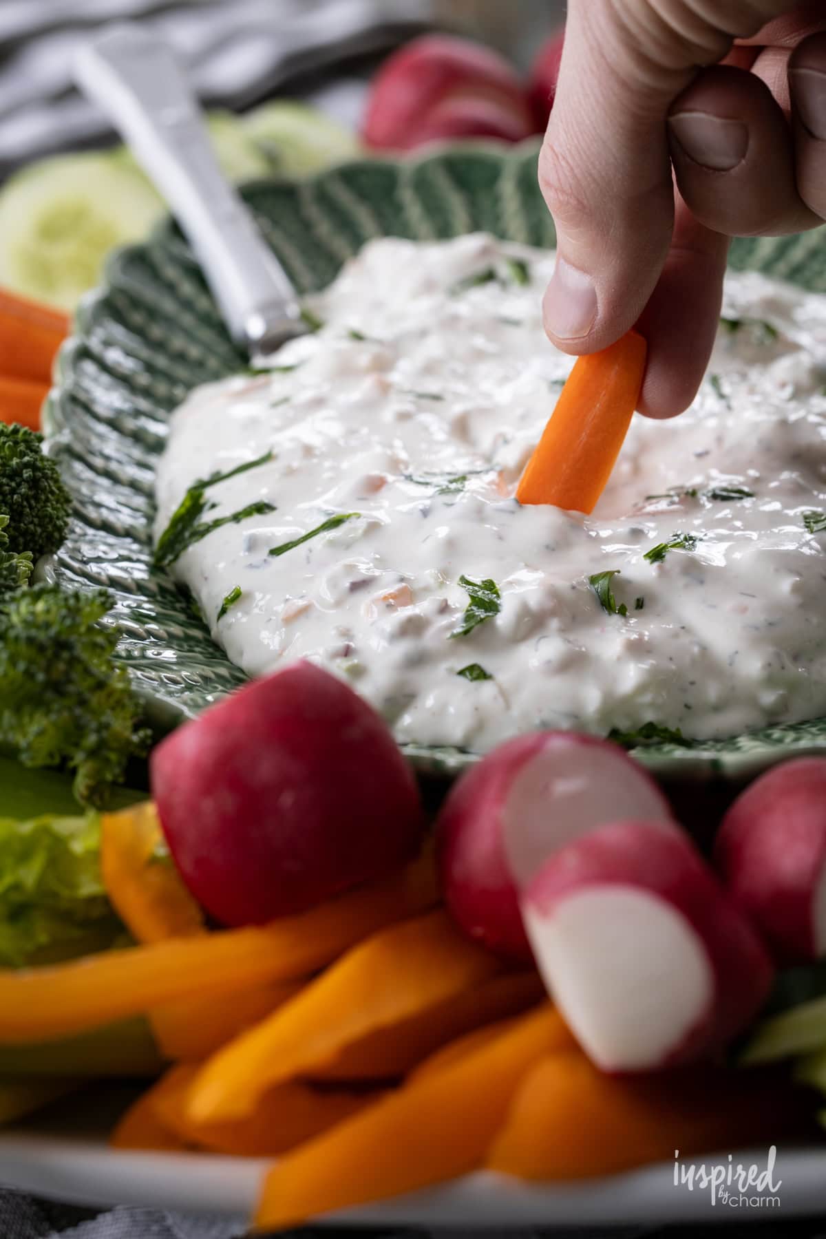 hand dipping carrot in creamy garden vegetable dip.