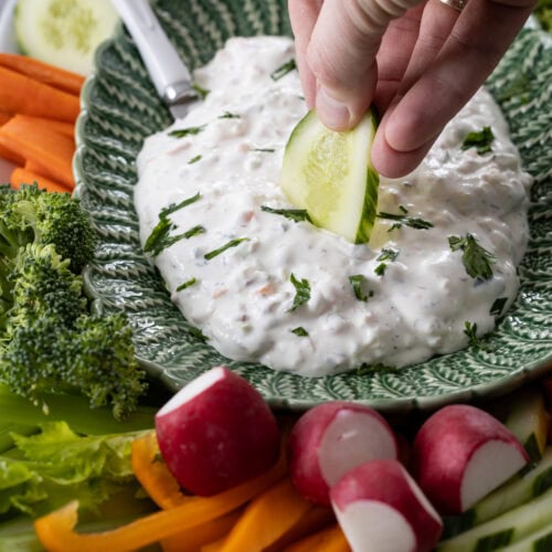 hand dipping cucumber into creamy garden vegetable dip.