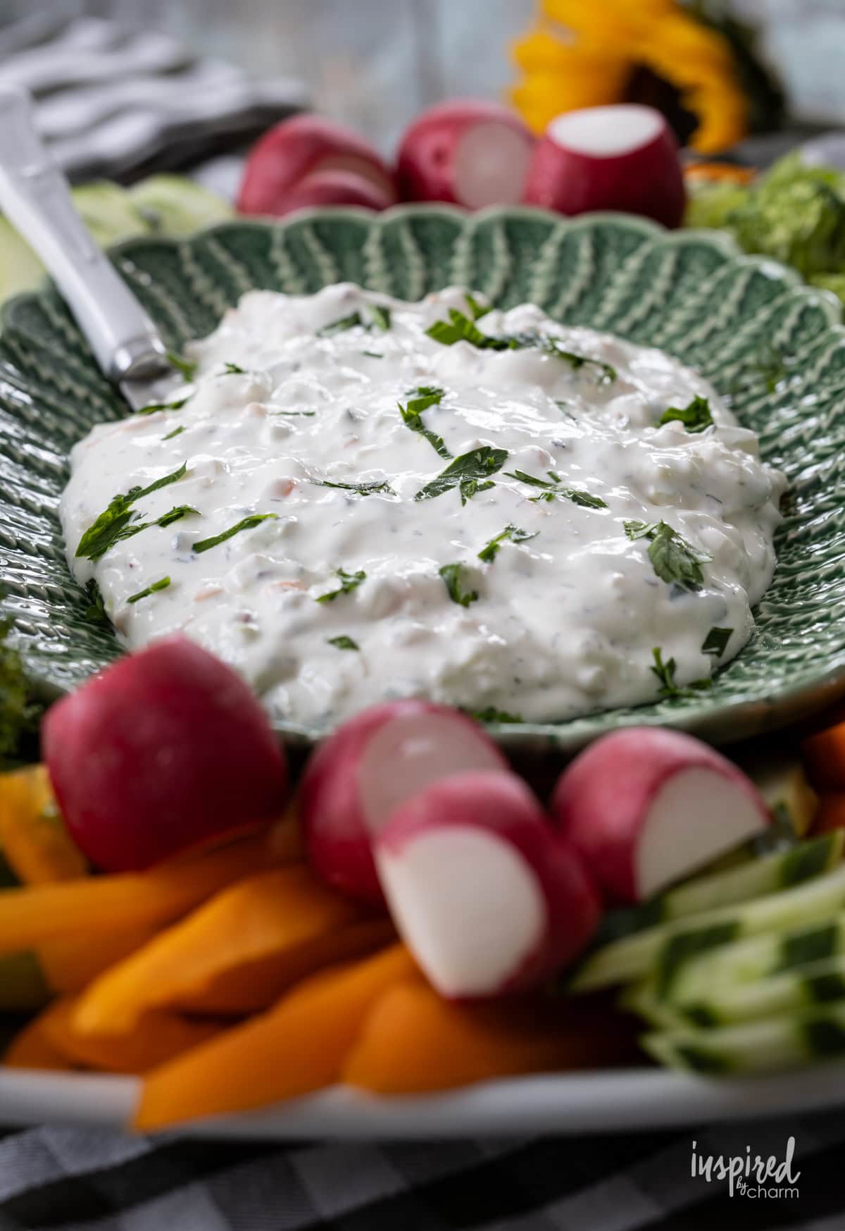 creamy garden vegetable dip in a green bowl with vegetables around it.