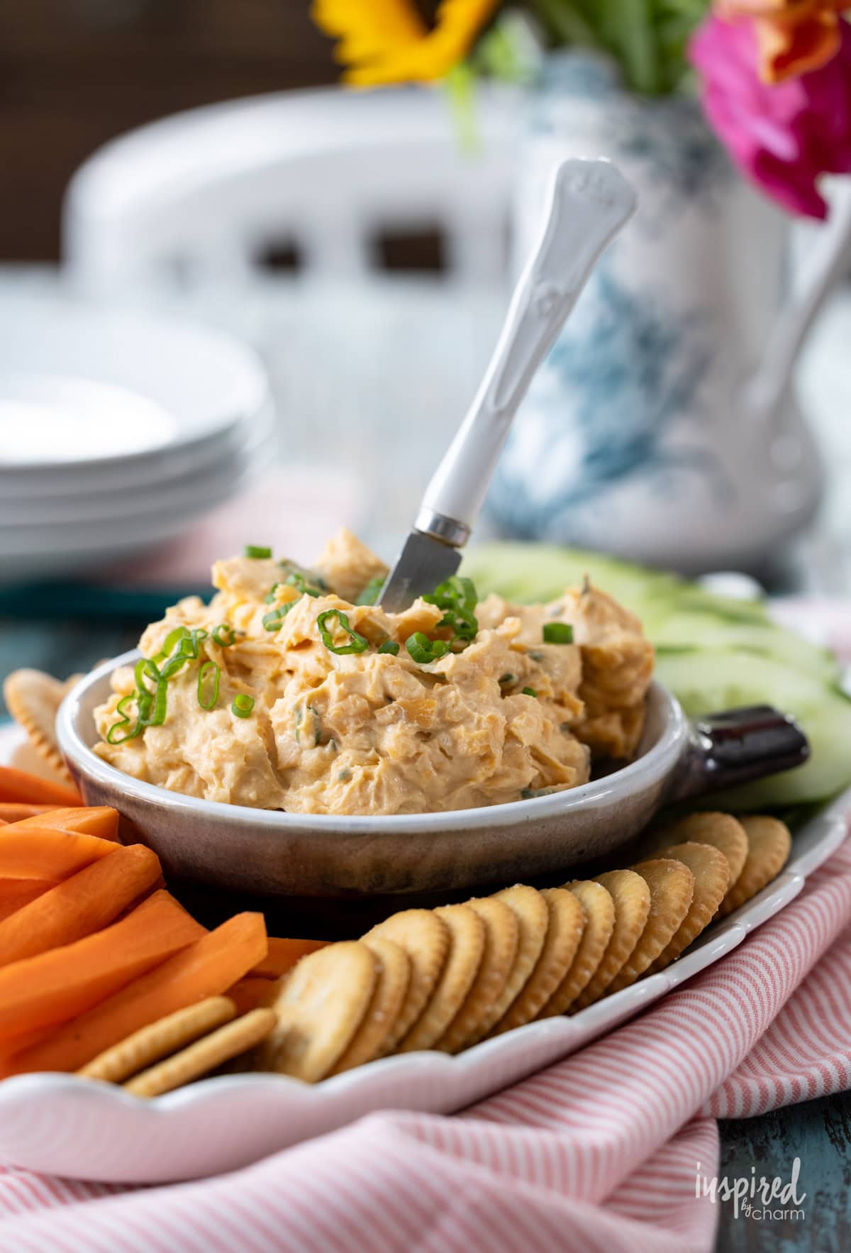 cheddar cheese dip in a bowl served with cut vegetables and crackers.