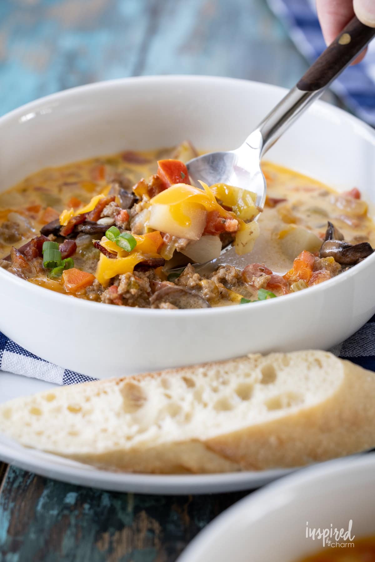hand holding a spoon with cheeseburger soup from in a bowl. 