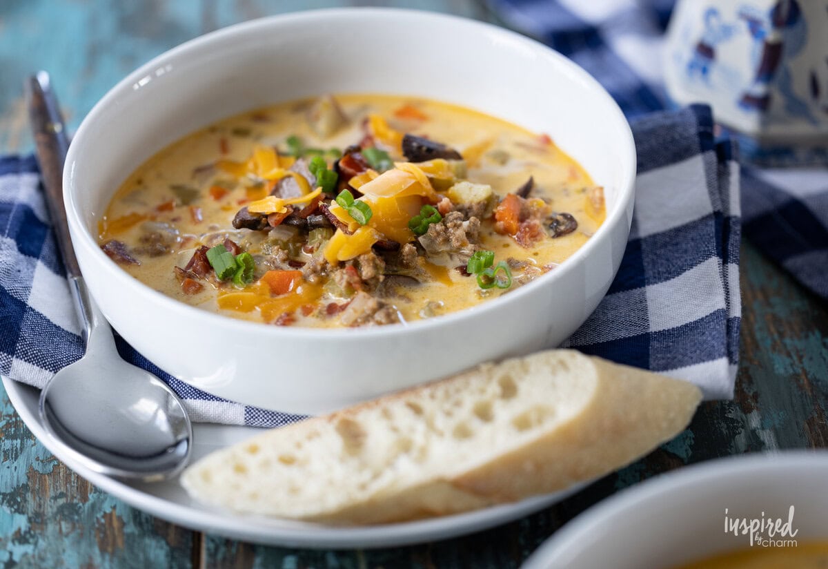 single bowl of cheeseburger soup with bread and a spoon on plate. 
