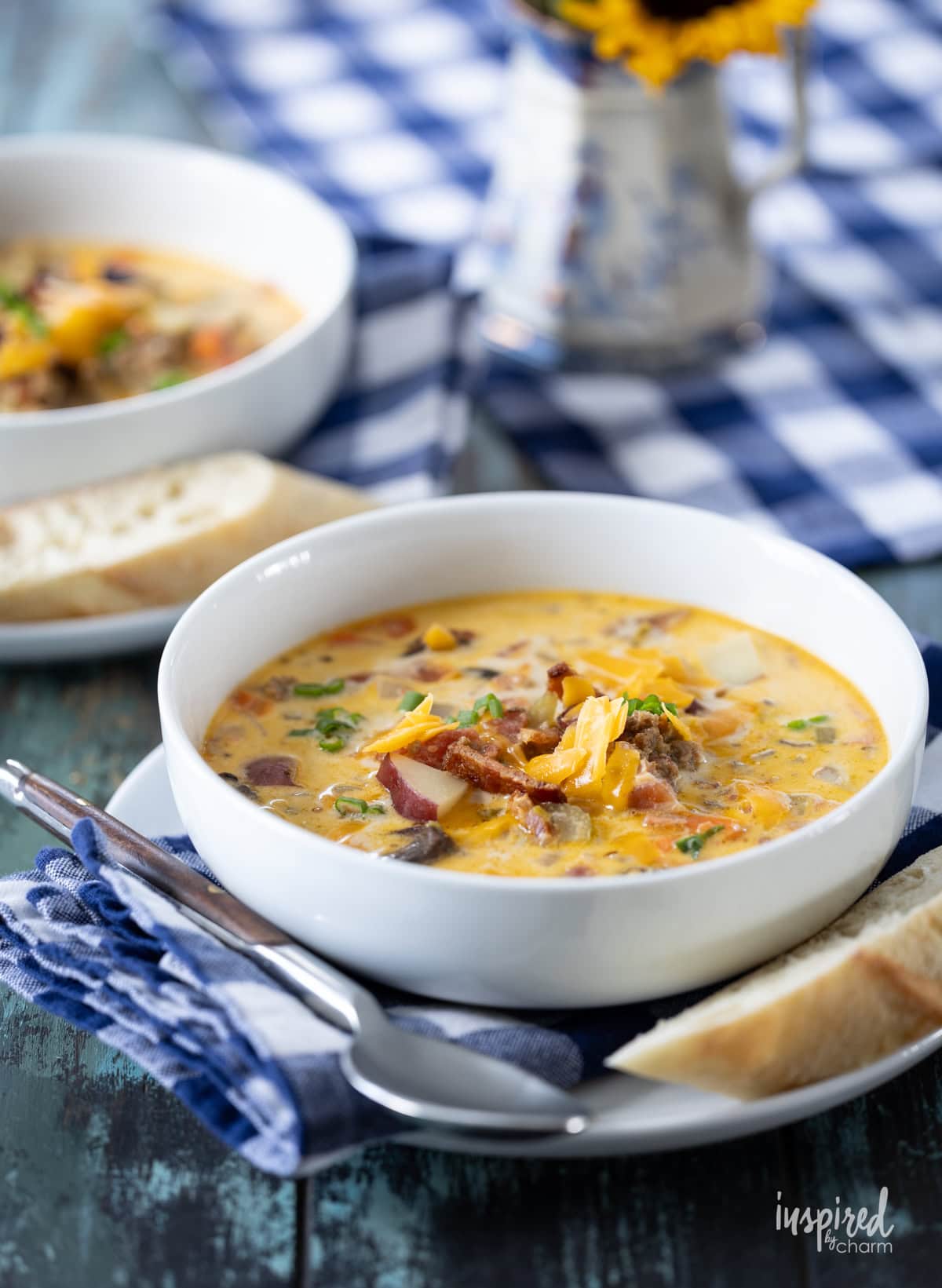 two bowls filled with cheeseburger soup  on a table with gingham cloth. 