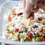 hand with chip taking a dip into greek feta layer dip.