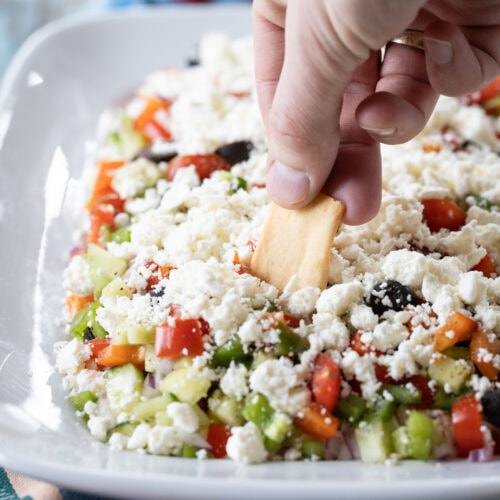 hand with chip taking a dip into greek feta layer dip.