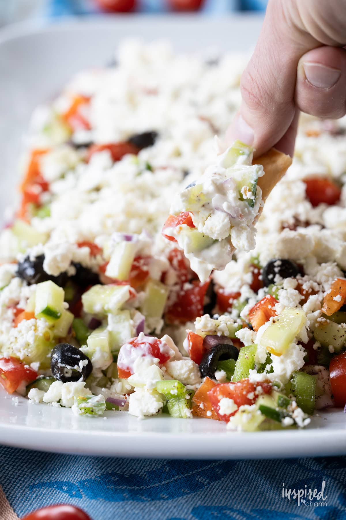 hand with pita chip taking a scoop of greek feta layer dip.