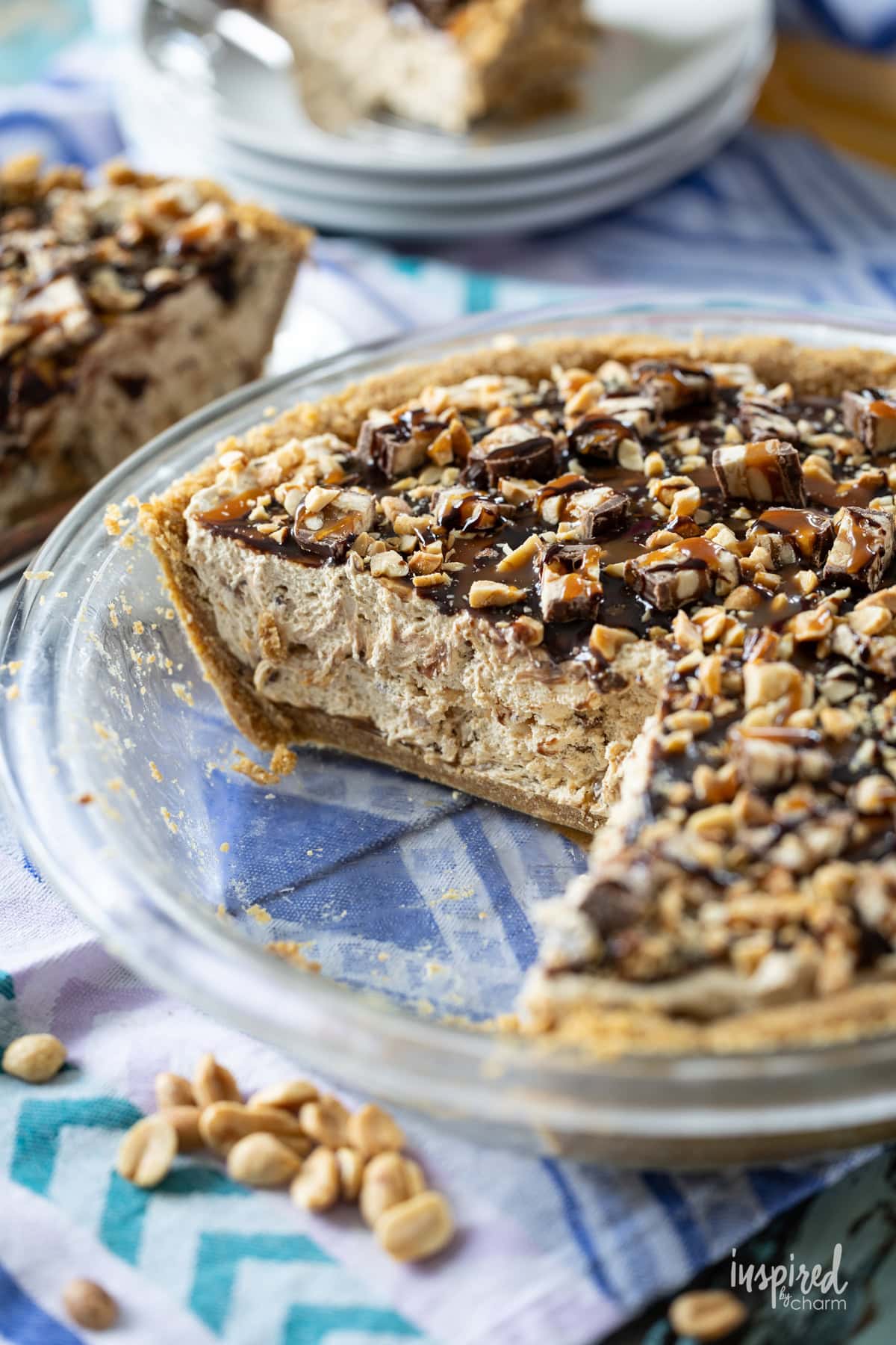 Peanut Butter Snickers Pie in glass pie dish with slices removed.