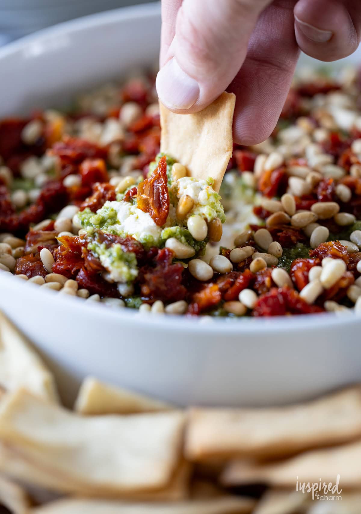 hand with pita chip dipping into Pesto and Feta Layer Dip.