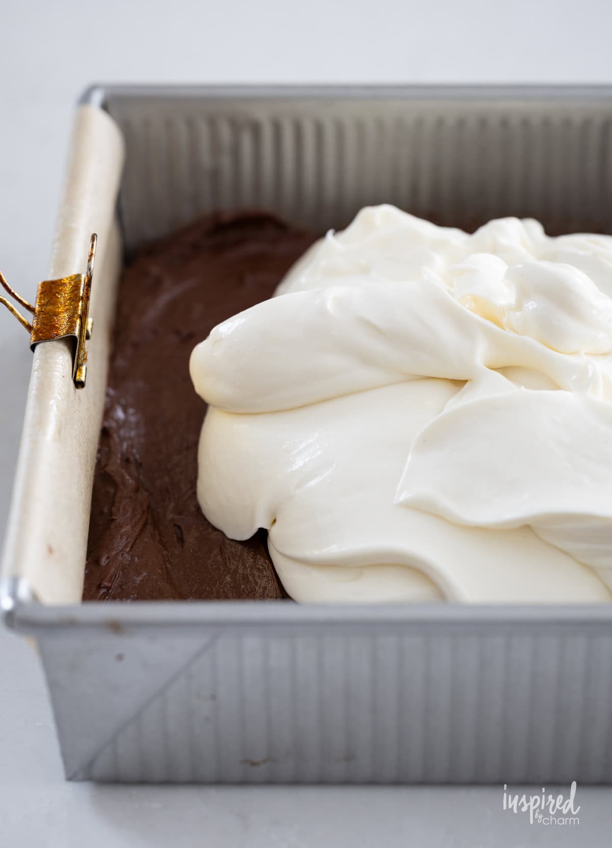 cheesecake batter over brownie batter in a square baking pan.