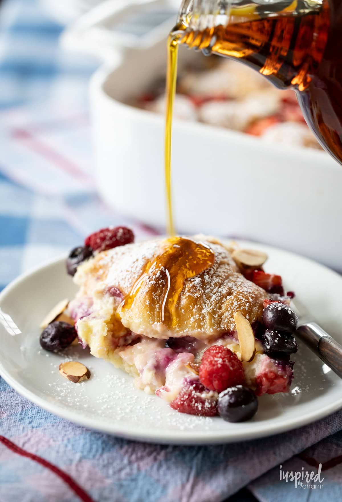 pouring maple syrup on piece of Mixed Berry Croissant Breakfast Casserole.