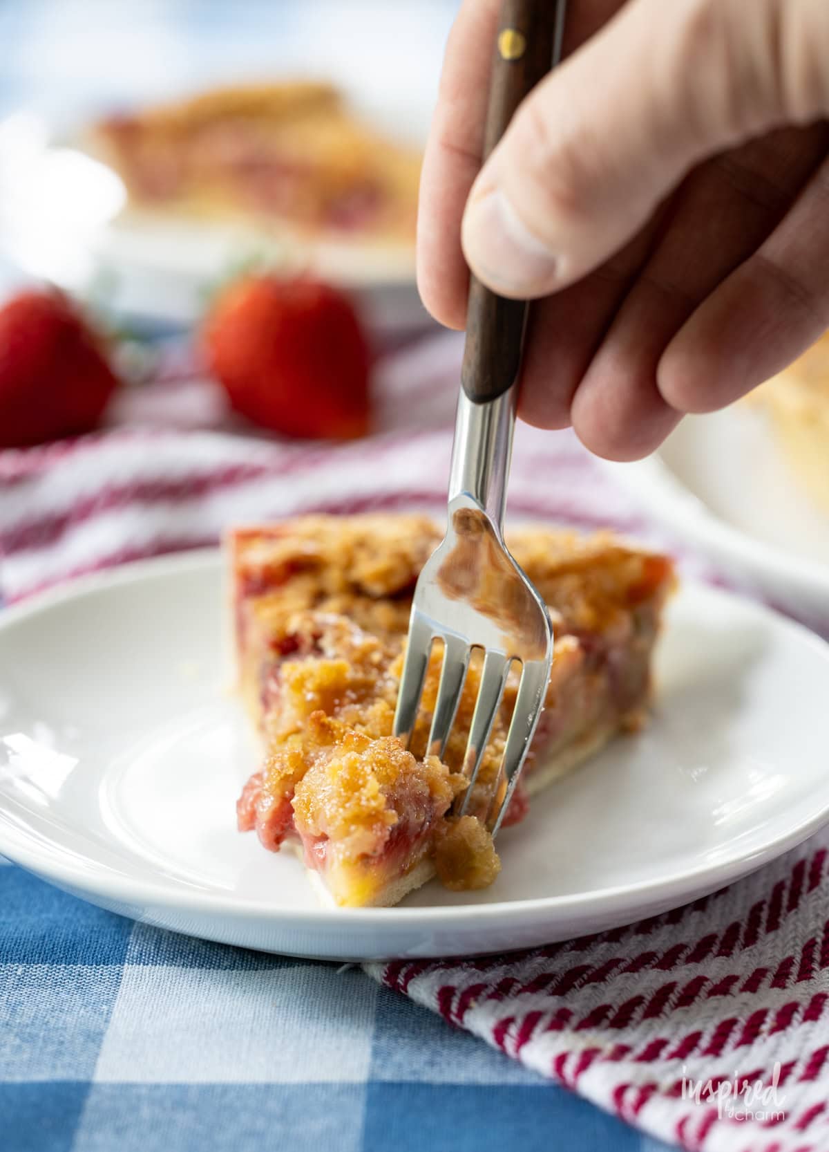 hand with a fork taking a bite of Strawberry Rhubarb Tart on plate. 