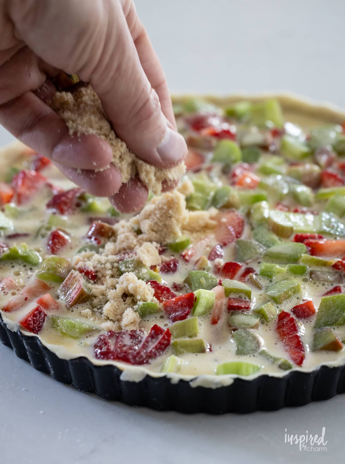 hand sprinkling crumble over strawberry and rhubarb tart. 